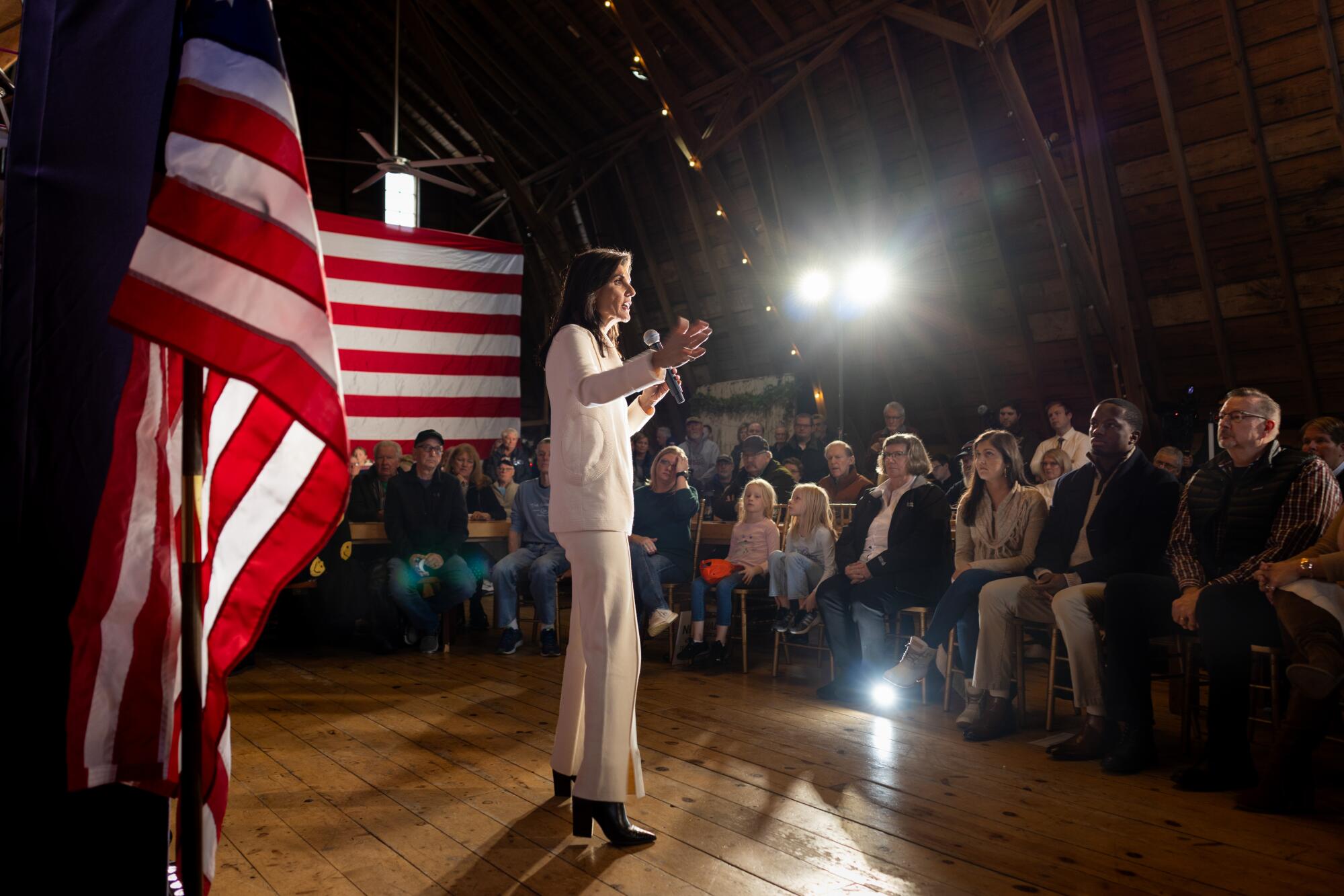 Nikki Haley speaks to voters in front of large American flags in Iowa.