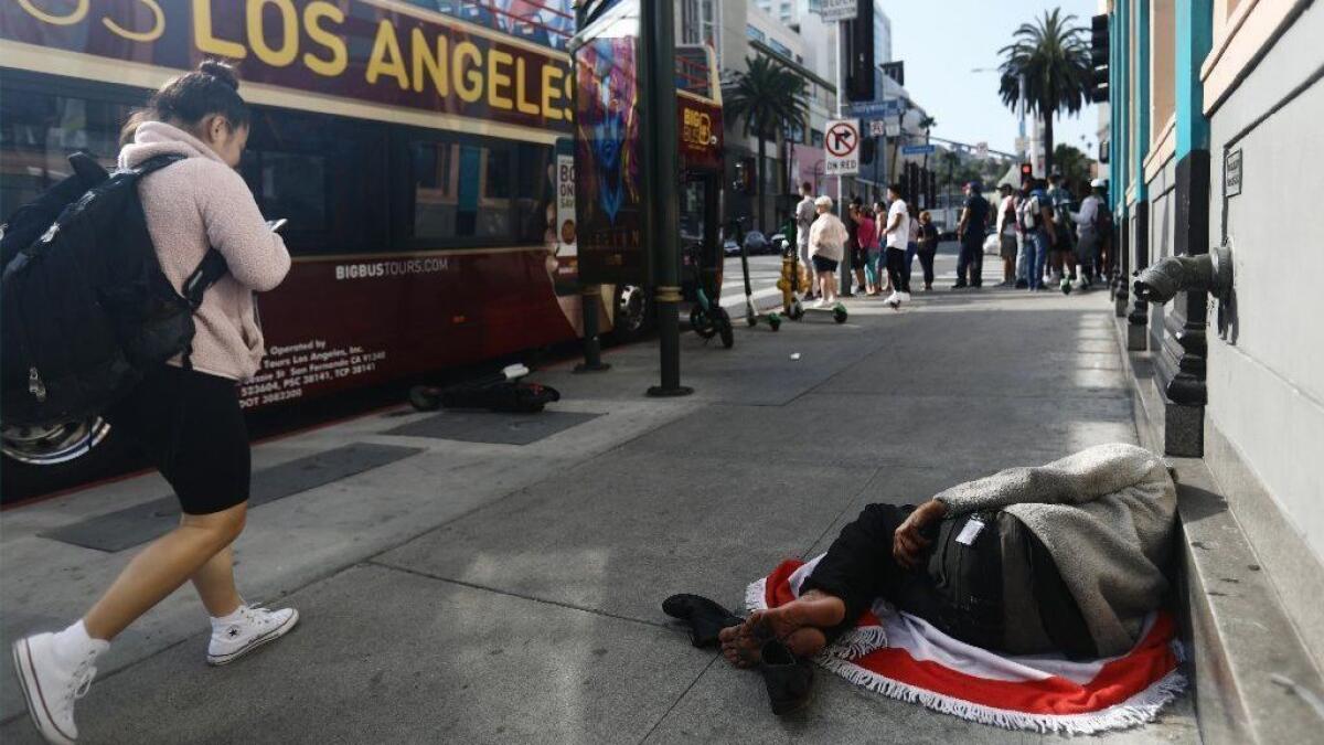 A man sleeps on the street near Hollywood Boulevard as a pedestrian and a tour bus pass by on June 6.