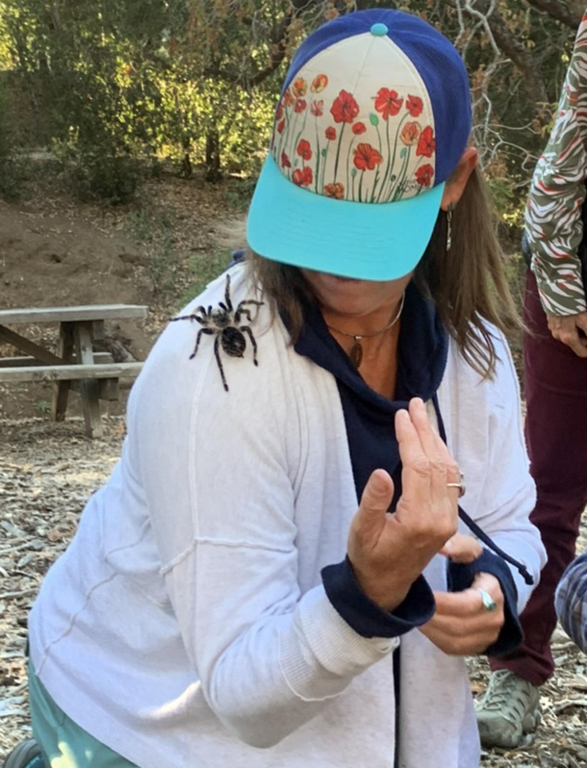 A woman in a ballcap turning her head to look at a tarantula on her right shoulder