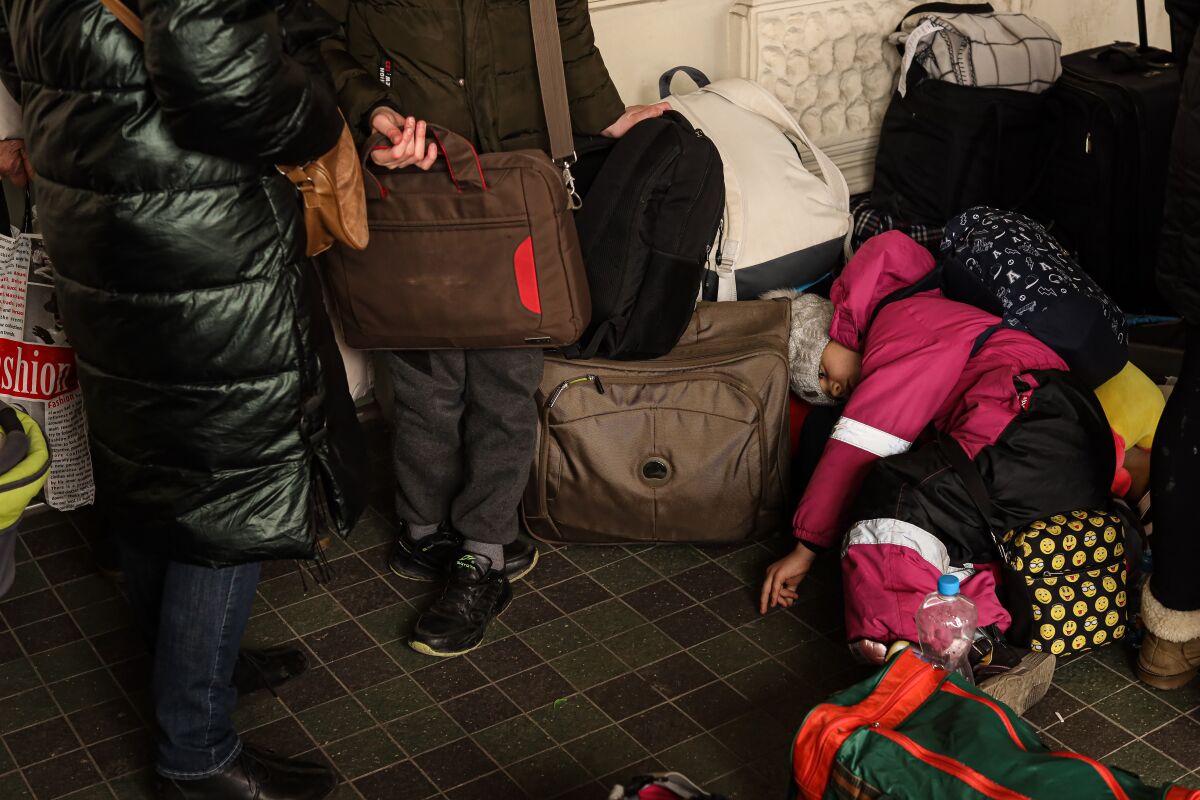 A child in pink winter clothing rests on luggage as other people stand nearby