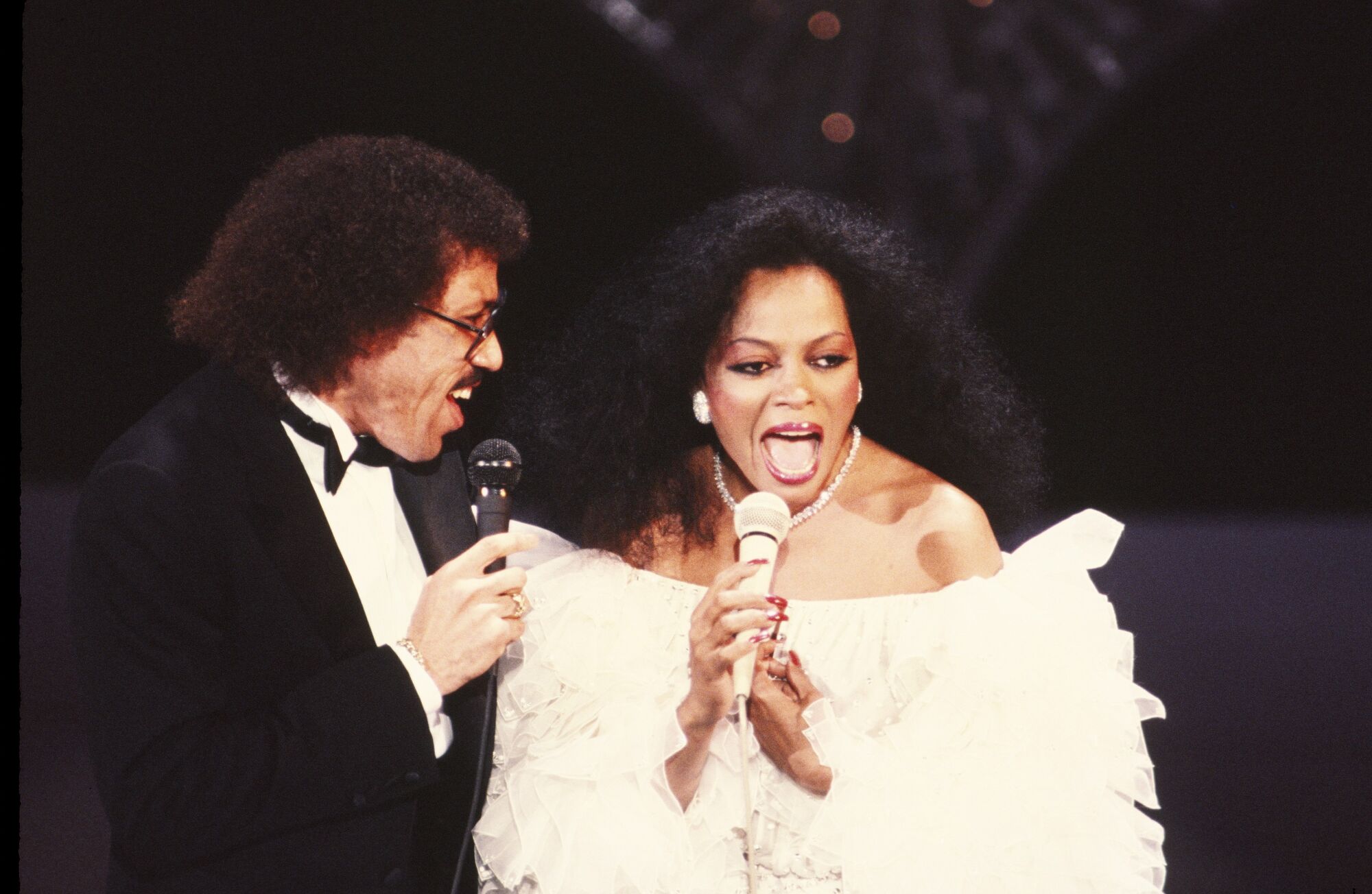 Lionel Richie, in a tux, and Diana Ross, in an evening gown, perform a duet on stage 