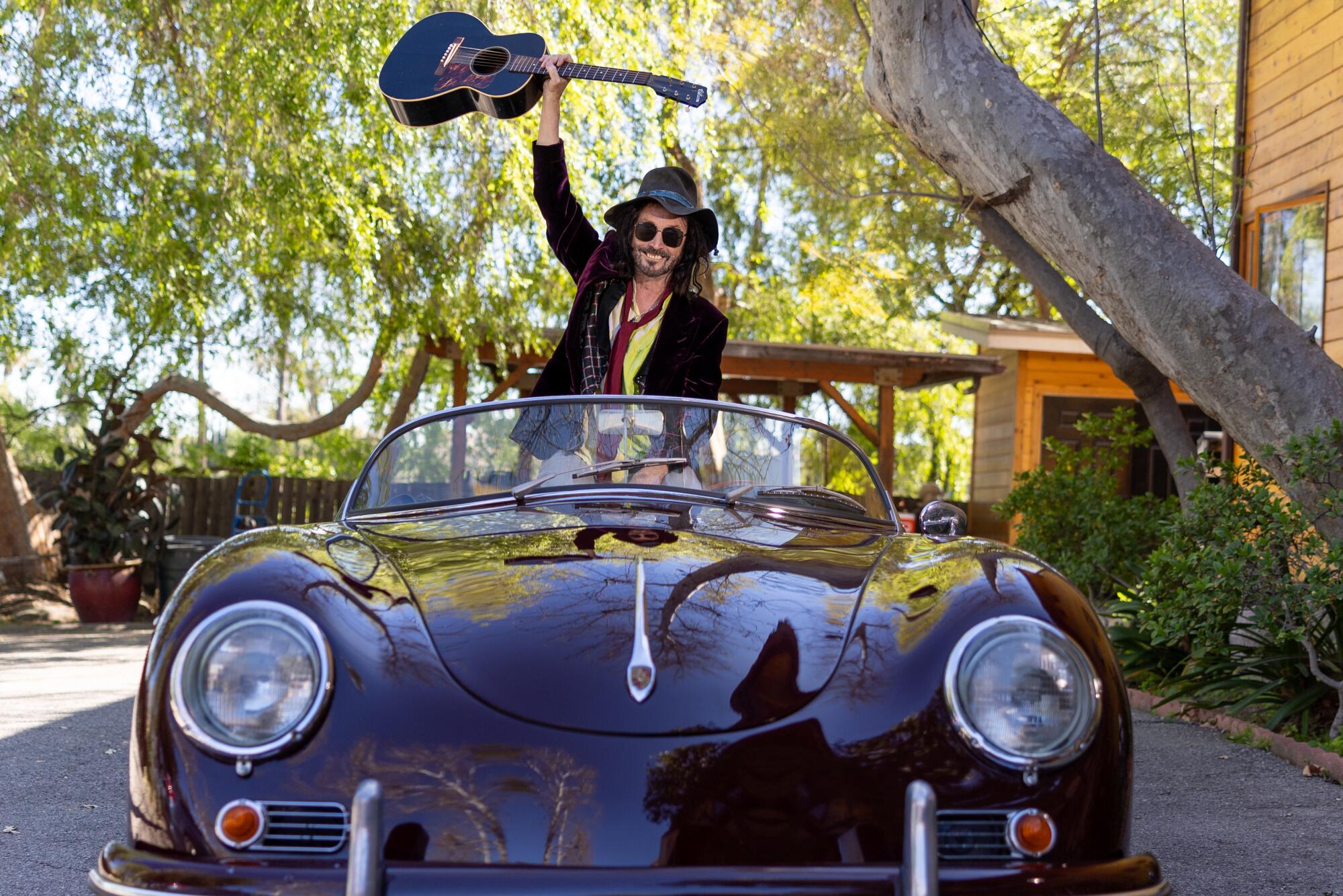 Mike Campbell sits up successful his classical Porsche and holds his guitar successful the air.