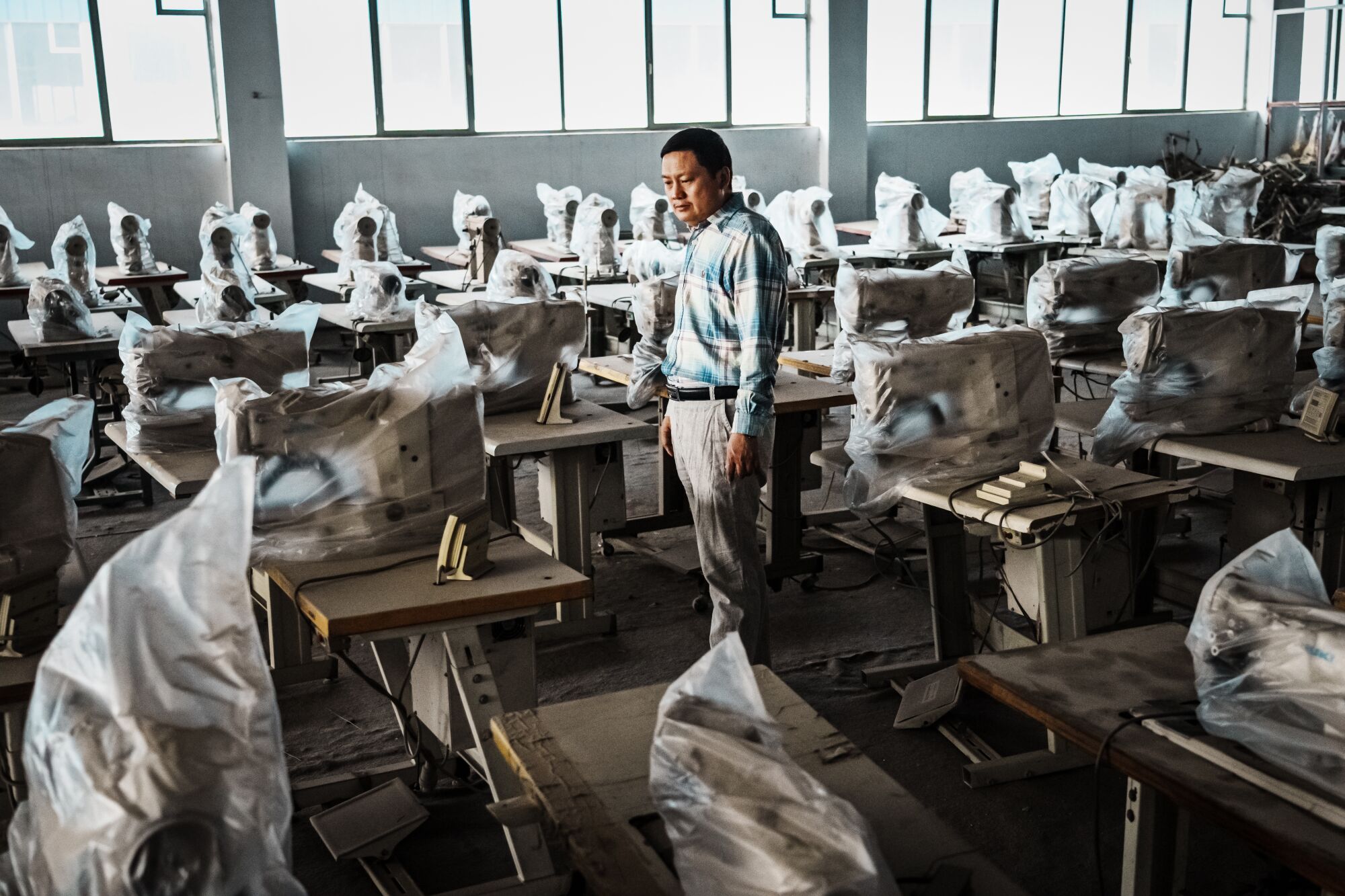 A man stands among sewing machines wrapped in plastic dust covers