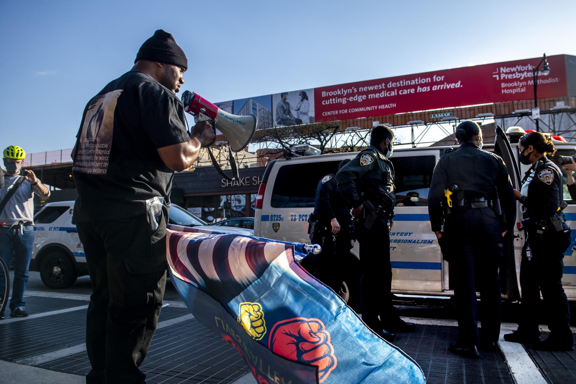 A man holds a bullhorn and flag nearby as police officers gather near a van 