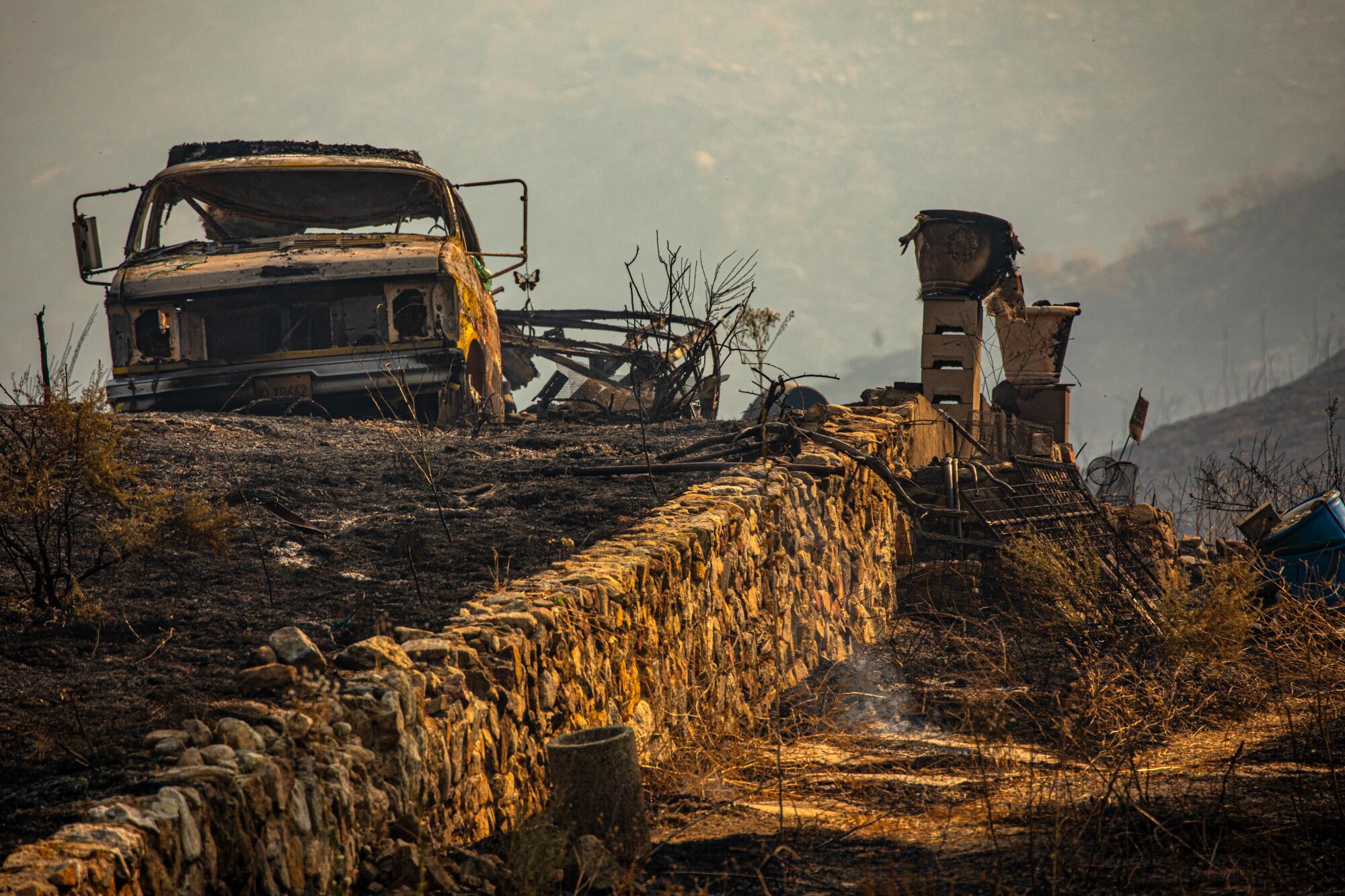 A burned out vehicle in an ashy landscape.