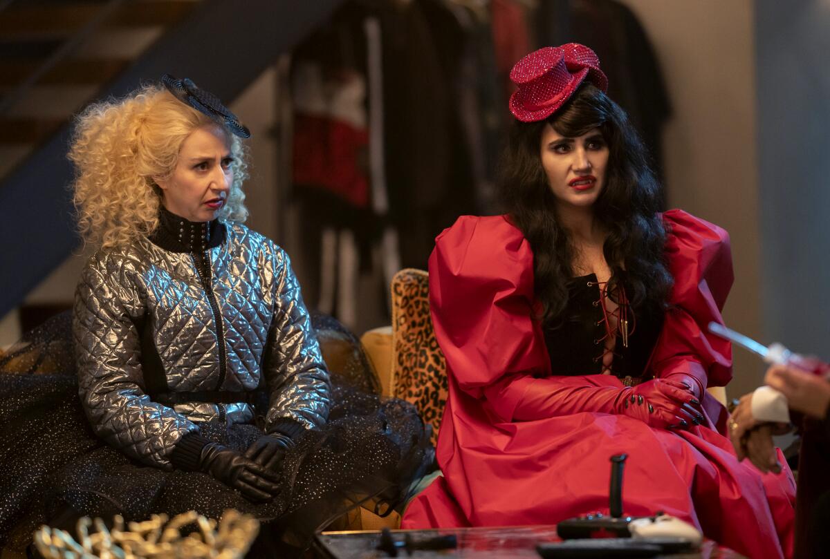 Two women sit in over-the-top outfits looking glum in a scene from "What We Do in the Shadows."