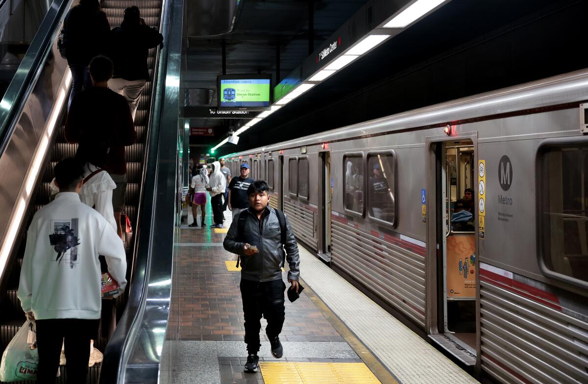 People go up an escalator or walk next to a subway car.