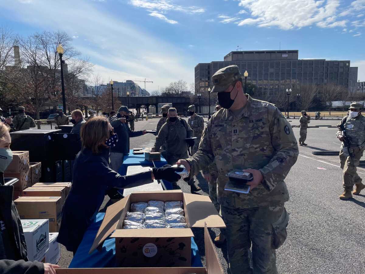 House Speaker Nancy Pelosi stands at a table with a box of packaged meals outside the Capitol.