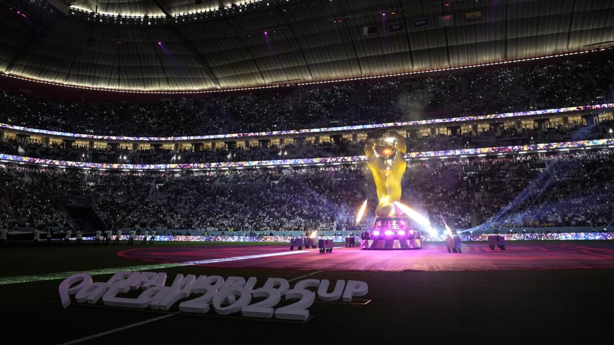 A large replica of the World Cup trophy is illuminated in a packed stadium.
