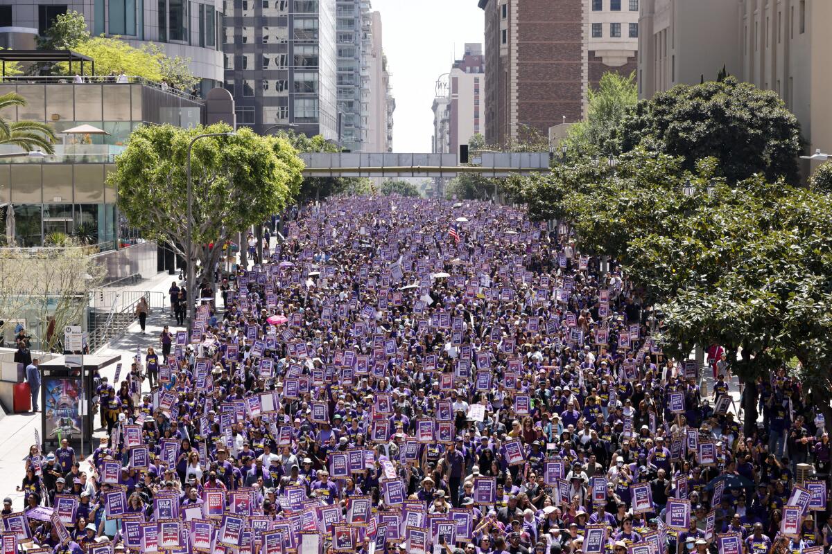 A sea of people line a street flanked by tall buildings