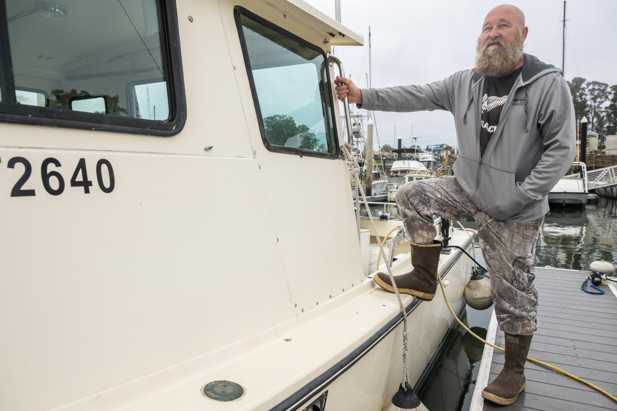 A bearded man with hoodie and boots standing on one boat and the other on the dock