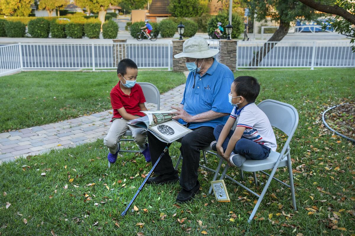 Charles Dirks reads to Luke Liu, 8, left, and his brother Eli, 6, in front of the Liu's home in Porter Ranch. 