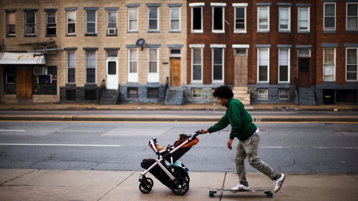 A man rides a skateboard and pushes his son in a stroller along a sidewalk in Baltimore on May 11.