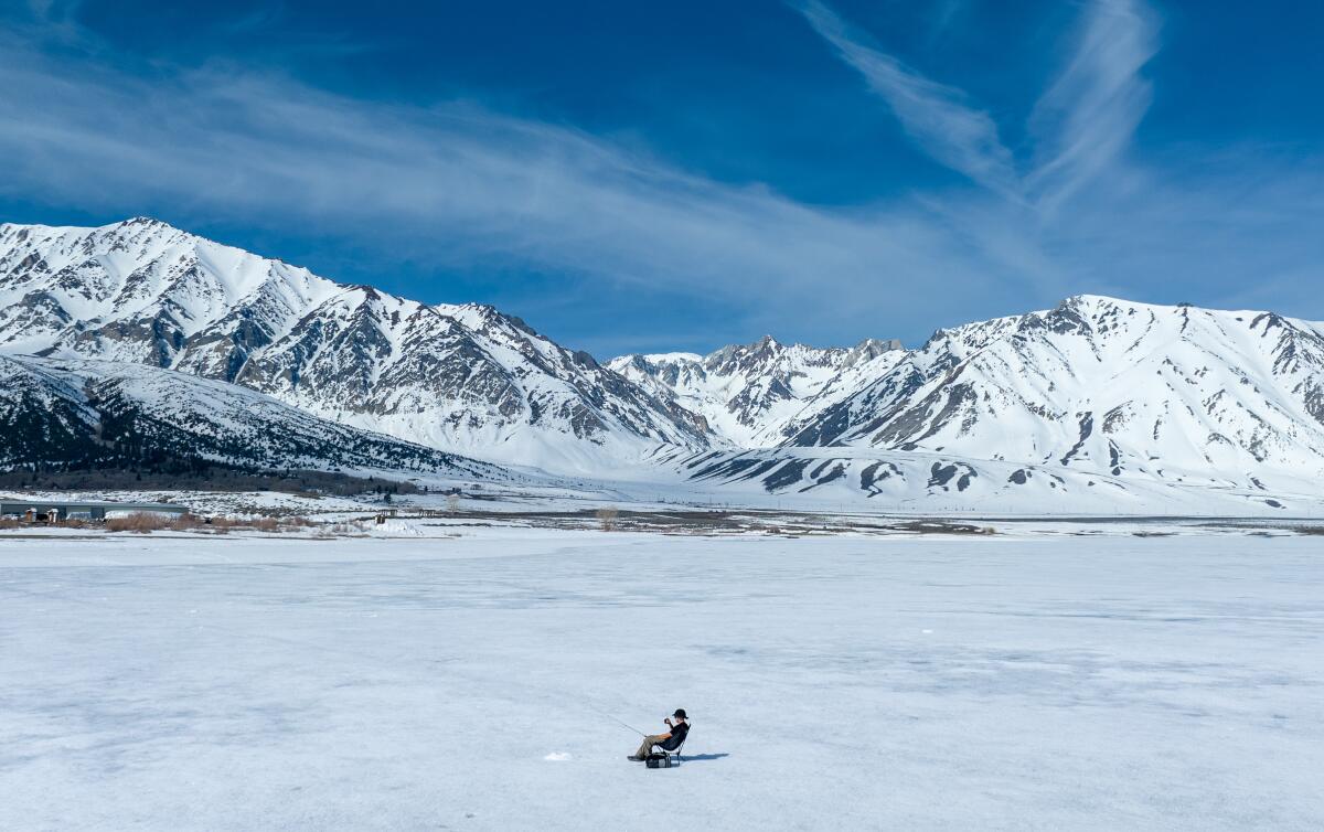 An ice fisherman waits for a bite as his line is dropped into a hole in a frozen Crowley Lake