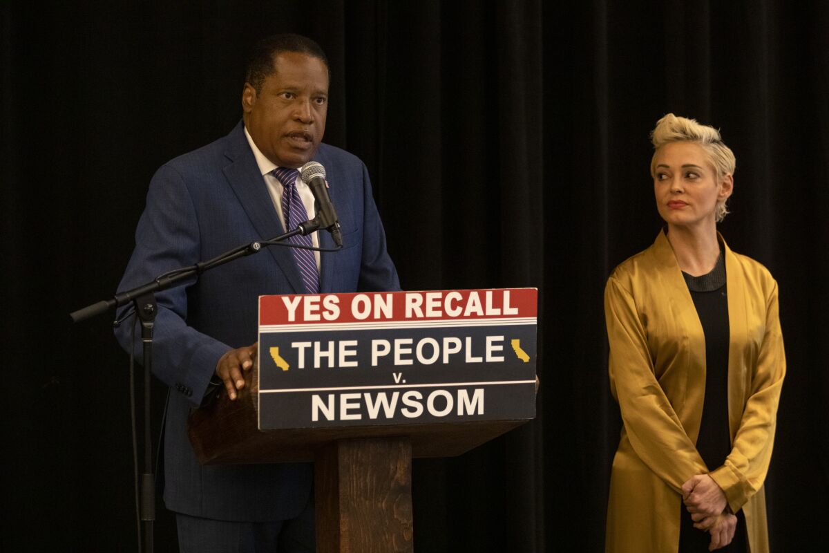 Larry Elder speaks at a podium next to Rose McGowan
