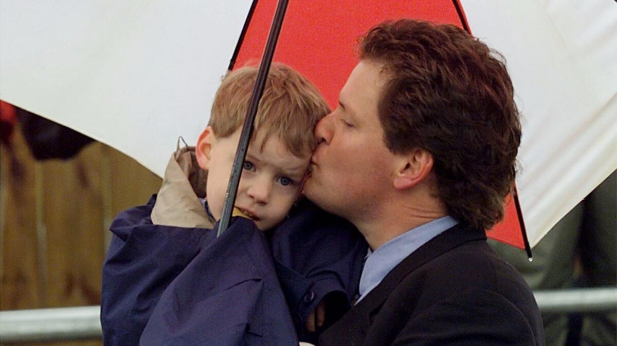 Roger Clinton, half-brother of President Bill Clinton, gives his son Tyler a kiss under his umbrella during the dedication ceremony of the former president's childhood home on March 12, 1999, in Hope, Ark.