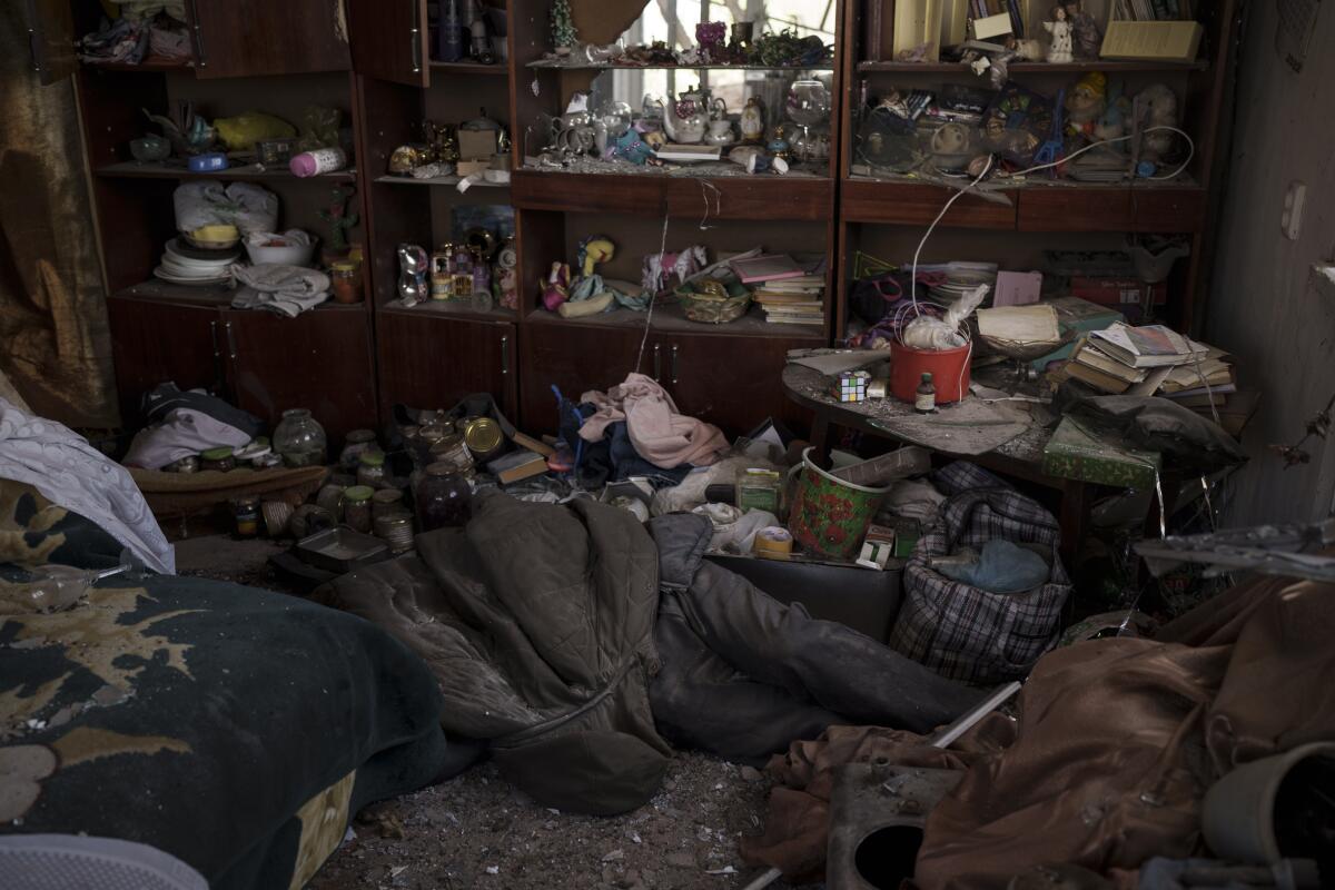 A body, its head and torso covered, lies near cabinets with books, a tea set and other personal possessions 