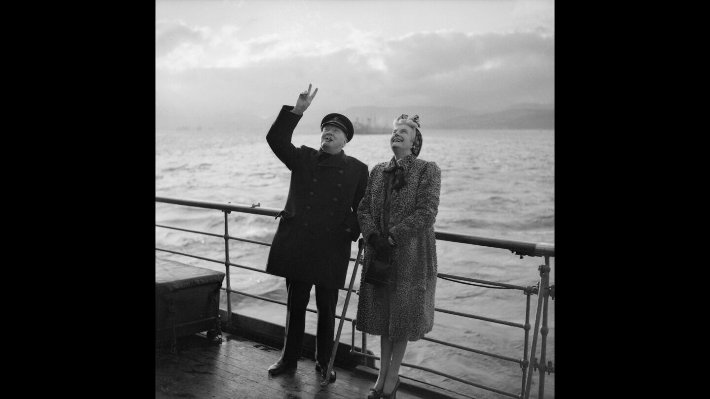 Prime Minister Winston Churchill. with wife Clementine, gives the 'V' sign in reply to troops from the Royal Navy as they cheer him aboard the Queen Mary in 1943.