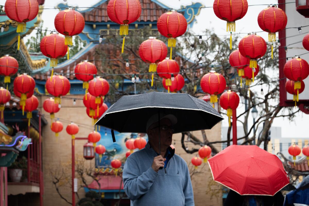 A man with his face covered by a black umbrella stands under red lanterns