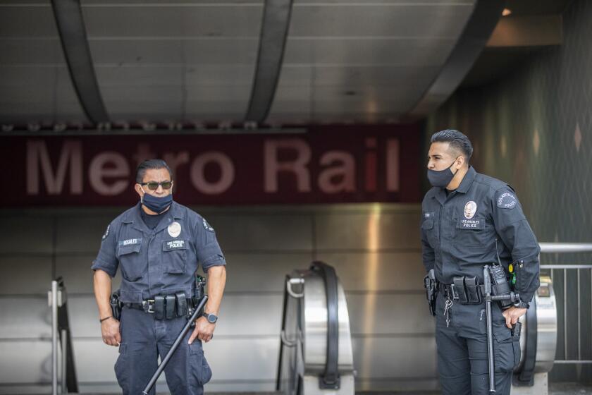 HOLLYWOOD, CA - JUNE 25: LAPD officers E. Rosales, left, and D. Castro, patrol the Metro Red Line Hollywood/Highland Metro Station as tourists pass by Thursday, June 25, 2020 in Hollywood, CA. The Metro Board of Directors held a meeting Thursday where the agenda included the consideration of appointing a committee to develop plans for replacing armed transit safety officers with ``smarter and more effective methods of providing public safety.'' Metro security is staffed by multiple agencies, including the L.A. County Sheriff's Department and L.A. and Long Beach police departments, transit security guards and contract security workers. (Allen J. Schaben / Los Angeles Times)