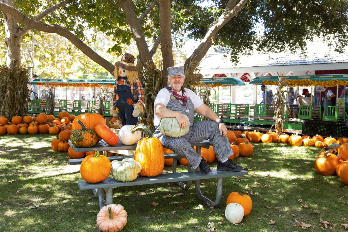 A man in overalls surrounded by pumpkins at Irvine Park Railroad's Pumpkin Patch.