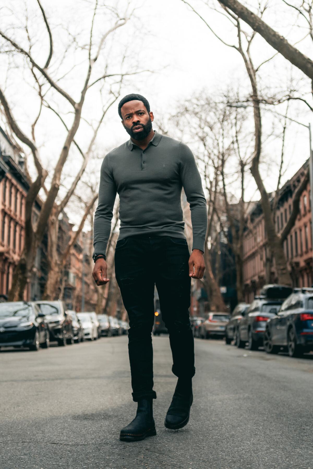 A muscular man stands in the middle of a street on a gray day.