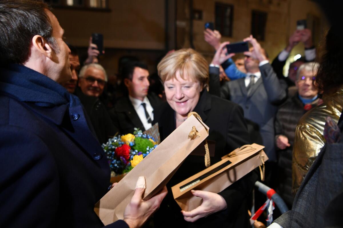 German Chancellor Angela Merkel and French President Emmanuel Macron, left, receive flowers and a bottle of wine as gifts as they are greeted by residents in Beaune, Burgundy, Wednesday Nov. 3, 2021. German Chancellor Angela Merkel will be feted by France in a special farewell ceremony honoring her leadership and partnership. Merkel is leaving office after 16 years in power. (Philippe Desmazes, Pool Photo via AP)