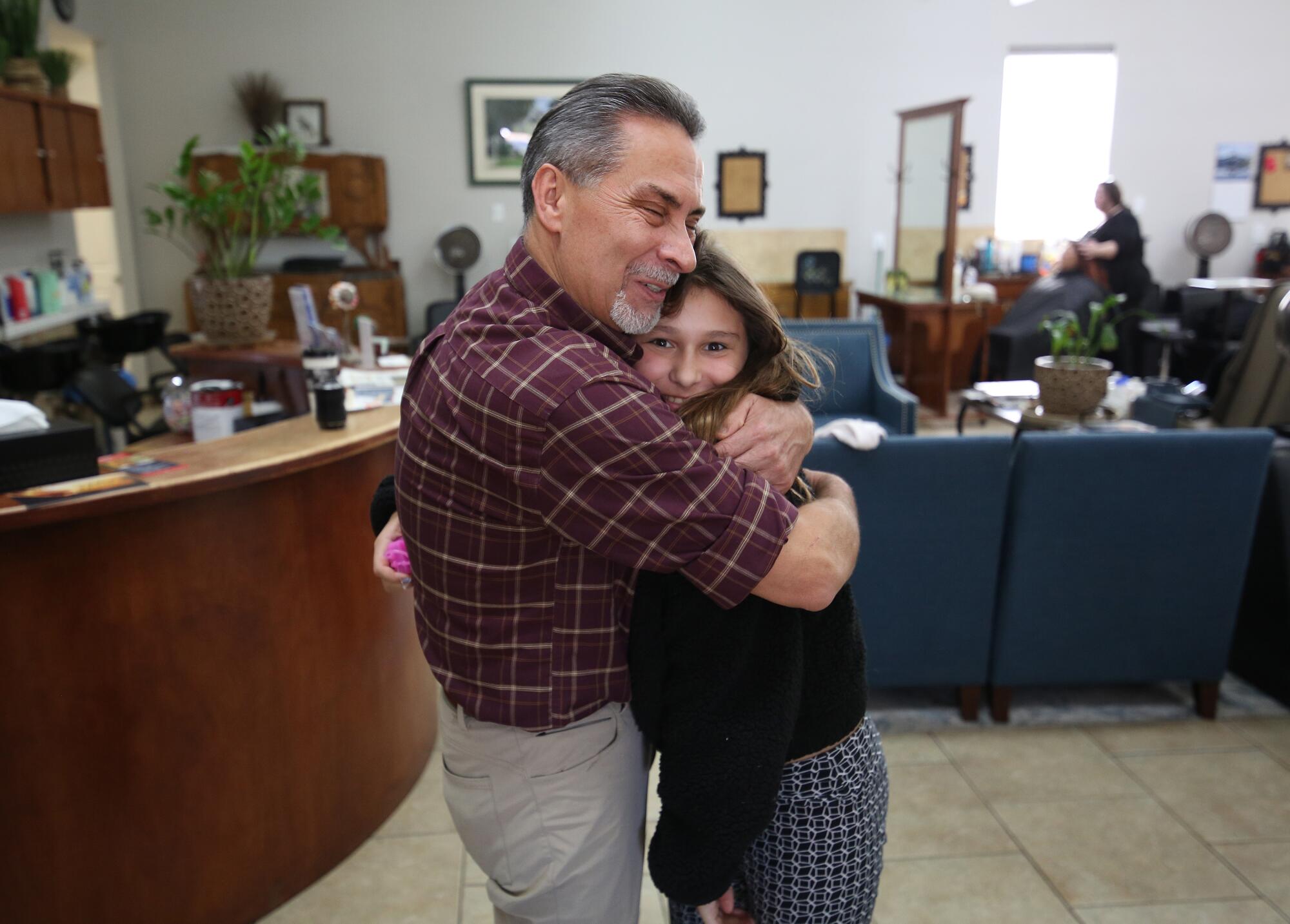 Adam Madeiros hugs his granddaughter Kamry Hudson at his salon