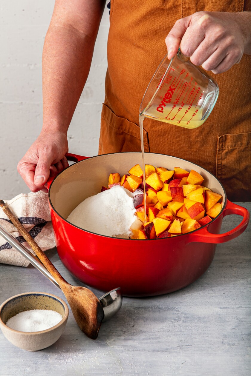 Lemon juice is poured into a pot with chopped fruit and sugar.