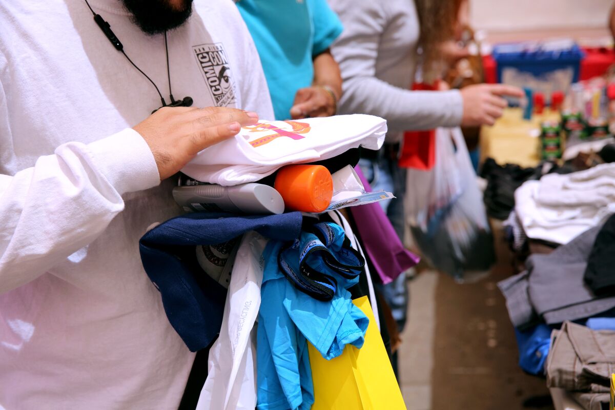 Men holding clothes and toiletries walk along a table of clothes.