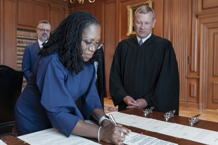 WASHINGTON, DC - JUNE 30: In this handout provided by the Supreme Court, Chief Justice John G. Roberts, Jr. (R) looks on as Justice Ketanji Brown Jackson signs the Oaths of Office in the Justices' Conference Room at the Supreme Court on June 30, 2022 in Washington, DC. Jackson was sworn in as the newest Supreme Court Justice today, replacing the now-retired Justice Stephen G. Breyer. (Photo by Fred Schilling/Collection of the Supreme Court of the United States via Getty Images)