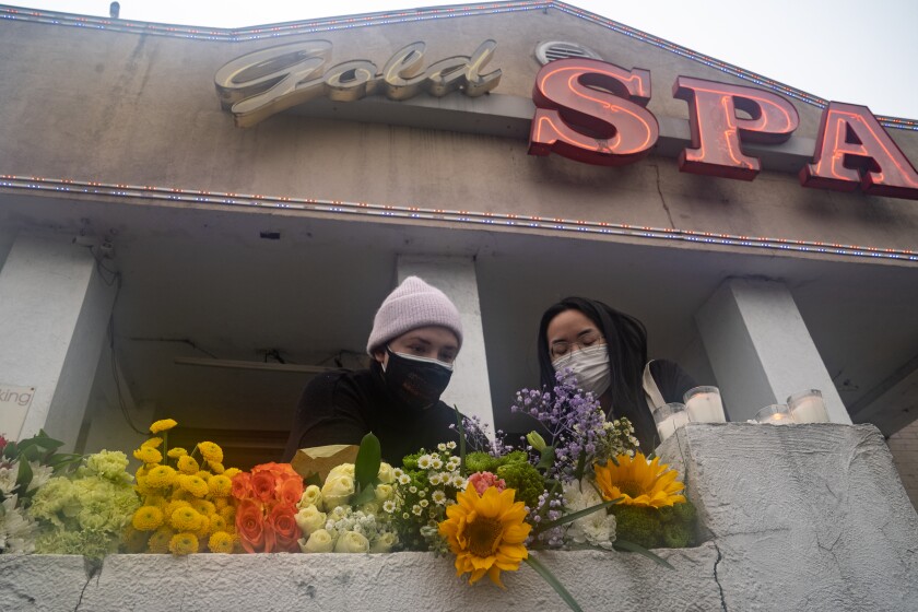 Two masked women leave flowers on a wall in front of Gold Spa in Atlanta. 