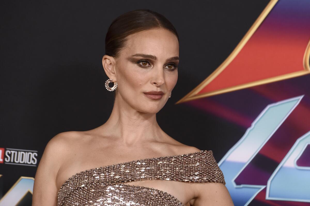 A woman with brown hair pulled back in a tight bun posing in a sparkly gold dress and earrings