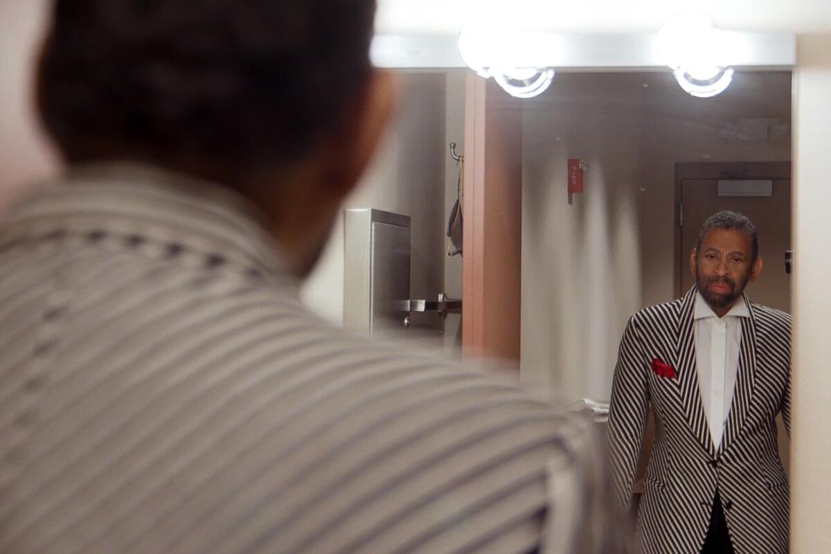 Maurice Hines, in a striped jacket, stands facing a dressing-room mirror