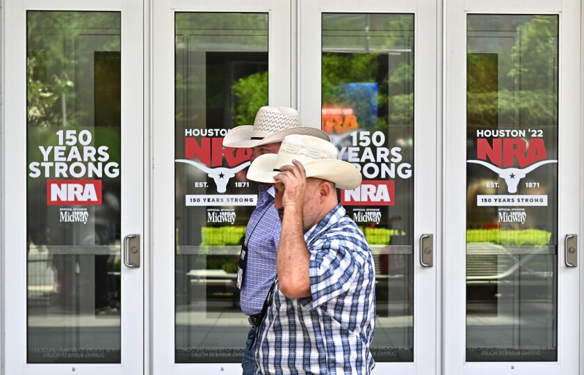 Zwei Männer mit Cowboyhüten gehen an Schildern vorbei "Houston'22 NRA" und "150 Jahre stark" am Eingang eines Gebäudes.