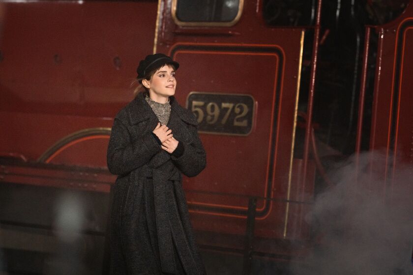 A woman in a hat and coat walking next to a red train
