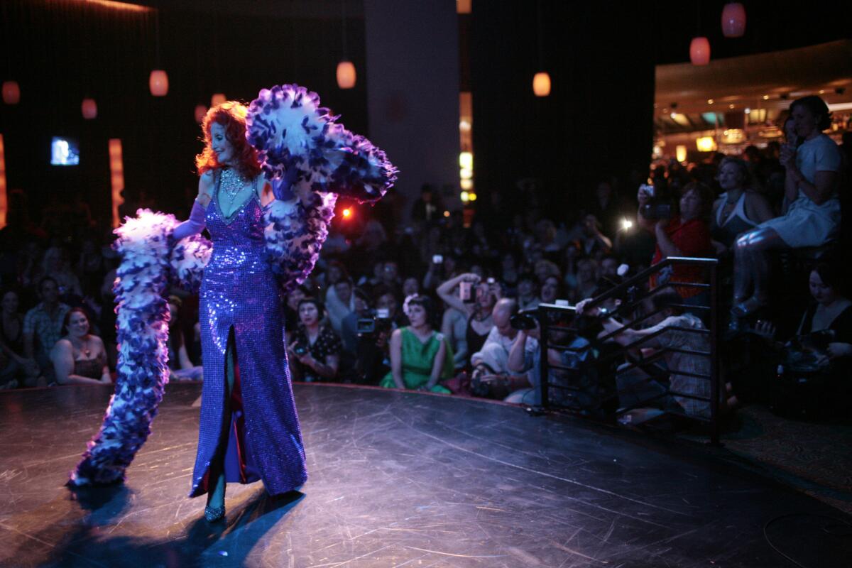Tempest Storm performs in a gown with a feather boa in front of a crowd