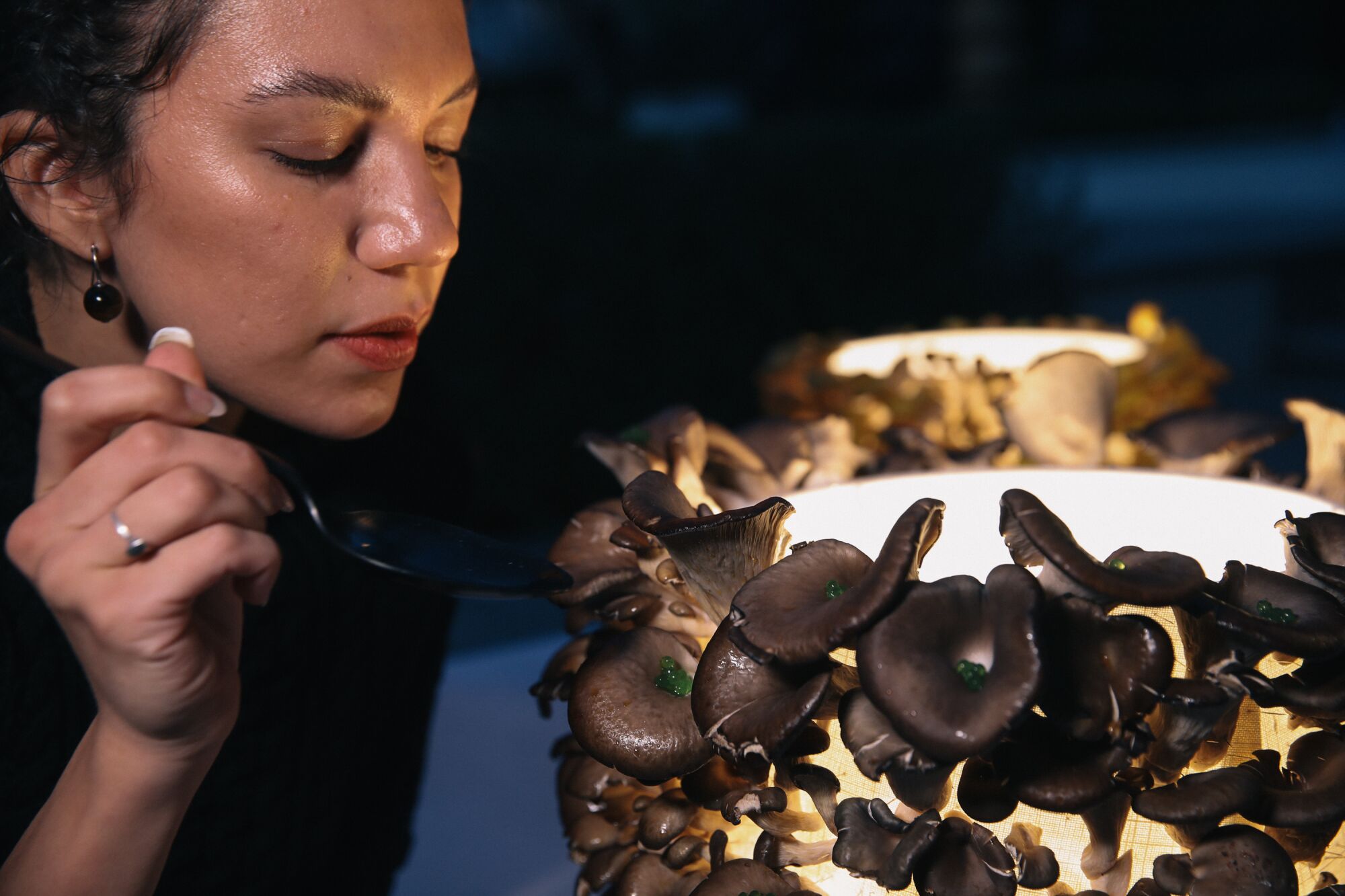 A woman spoons "algae" caviar onto oyster mushrooms for a mushroom-and-light installation.