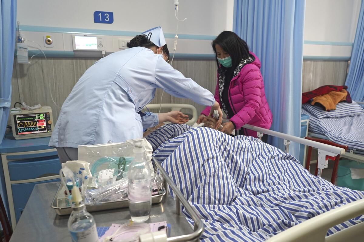 A nurse and a woman in a coat stand on either side of a hospital bed.