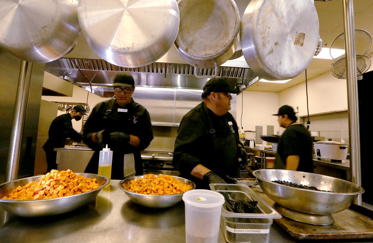 Interns in black chef uniforms prepare Mexican dishes in a kitchen.