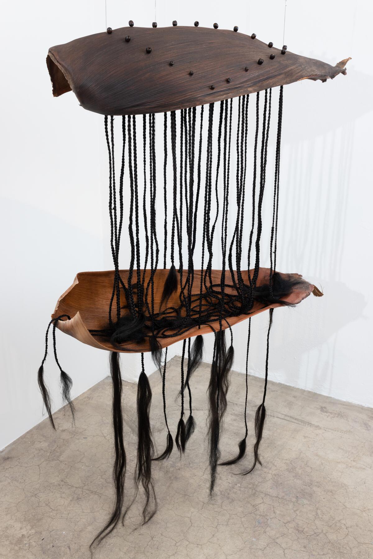 A hanging sculpture made of palm leaves, synthetic hair and wood beads.