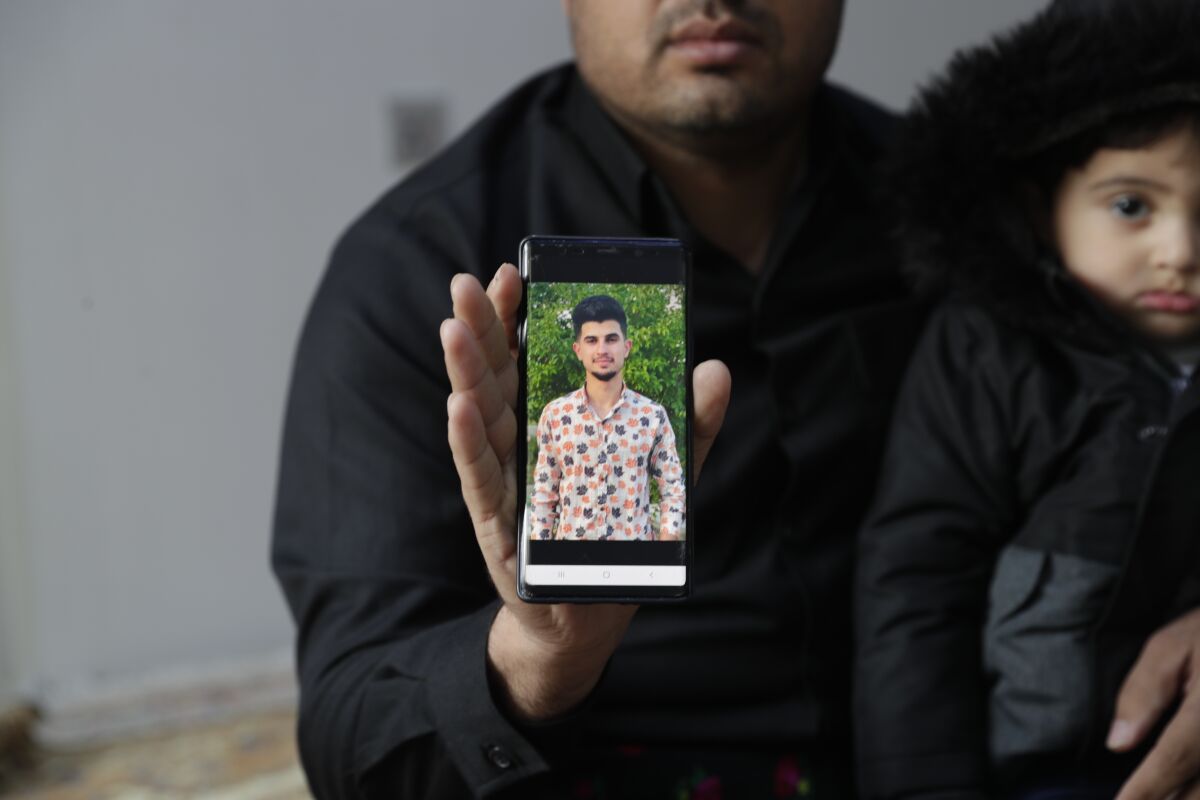Zana Mamand, shows a photo of his missing brother, Twana Mamand, who was lost at sea in the English Channel trying to get to the UK, sits with family members, at the family house in Ranya, Iraq, Tuesday, Nov. 30, 2021. Twana had tried and failed five times to cross the English Channel from Calais before he boarded a small boat on the evening of Nov. 23. (AP Photo/Khalid Mohammed)