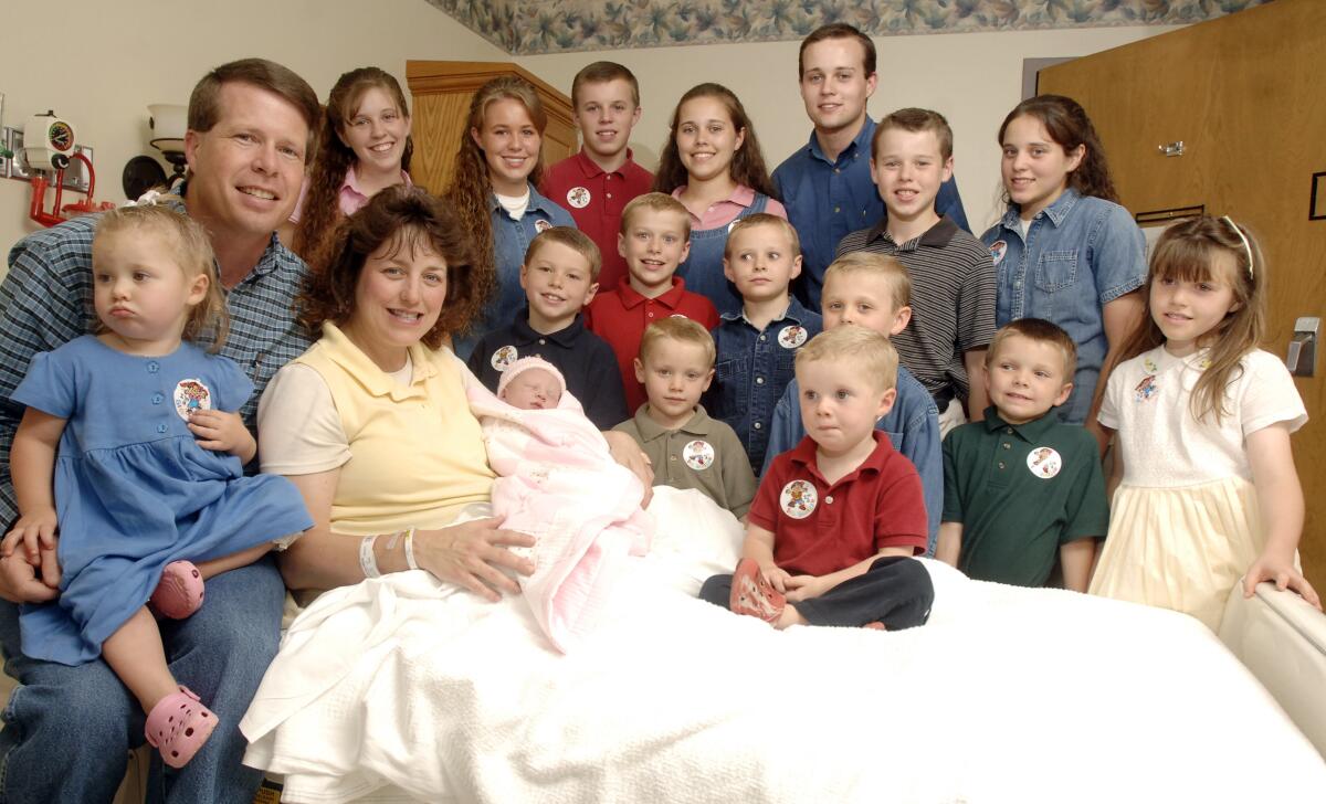 A woman sits in a hospital bed holding an infant and surrounded by 16 children and her husband