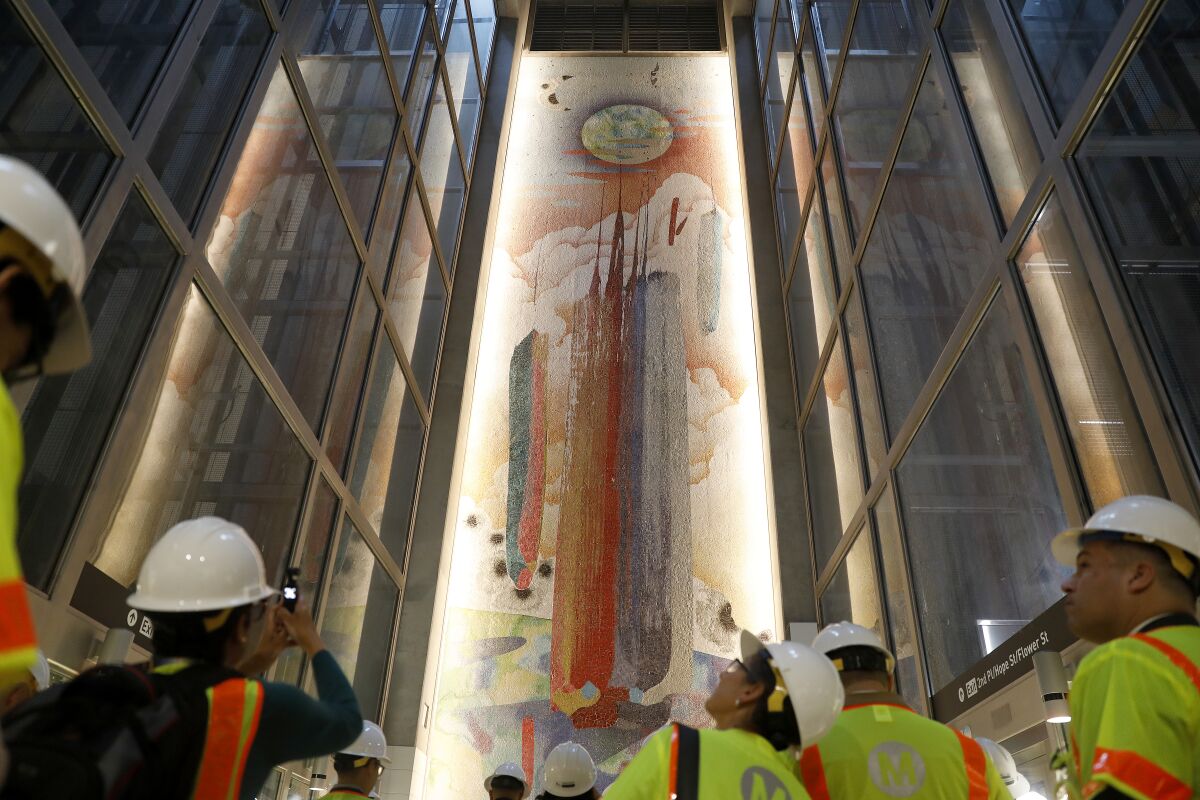 People in white hard hats and neon vests look up at artwork soaring above them 