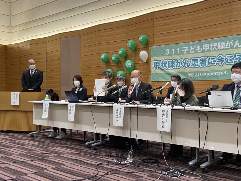 Flanked by other lawyers, a plaintiff and the mother of another, lawyer Yuichi Kaido, third from left, shows a court document filed on behalf of six people with thyroid cancer and the connection to radiation leaked from the 2014 Fukushima nuclear power plant accident with the Tokyo District Court during a news conference, Thursday, Jan. 27, 2022, in Tokyo. Banner in rear reads "support now for thyroid cancer patients." (AP Photo/Mari Yamaguchi)