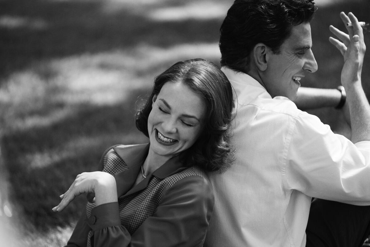 Black-and-white photo of Carey Mulligan smiling wide and leaning on Bradley Cooper's back.