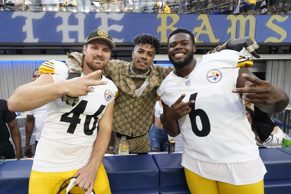 Steelers players Christian Kuntz, left, and Pressley Harvin III, right, flank rapper Blueface as he leans over a blue barrier