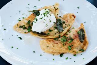 A trio of large cheese-and-potato pierogi topped with sour cream and herbs on a white plate at Bar Sinizki.