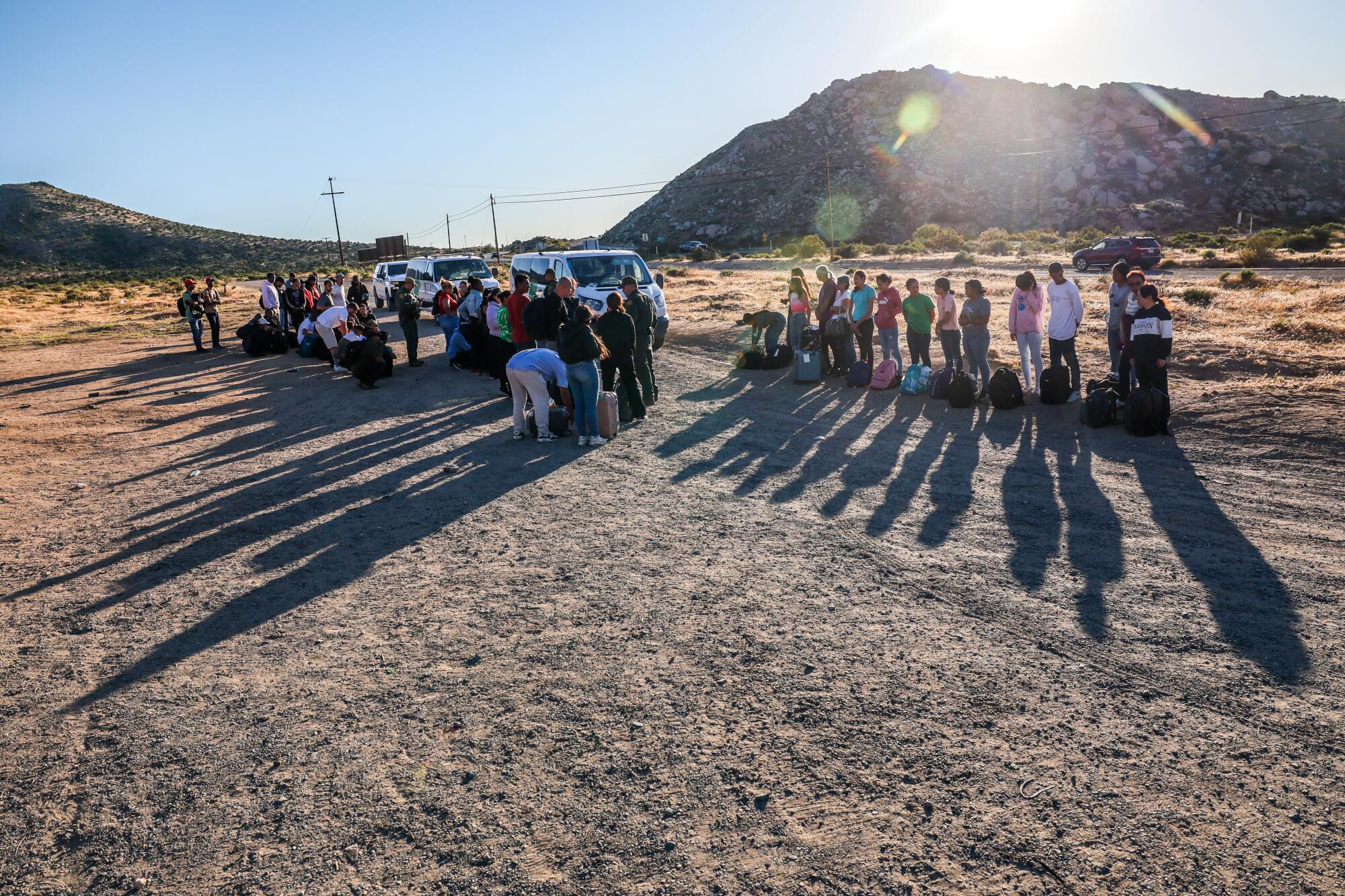 People line up on a desert landscape with a small mountain behind