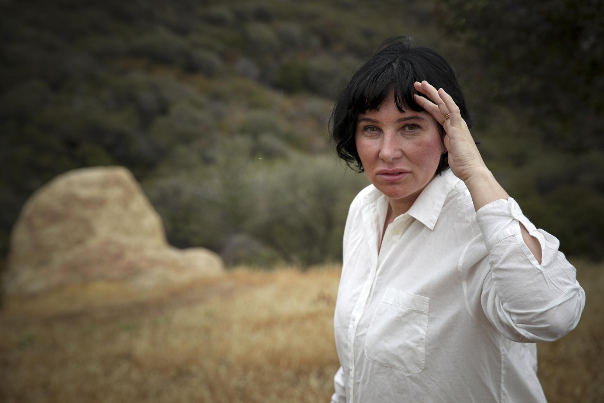 A woman stands amid the greens and browns of a canyon.